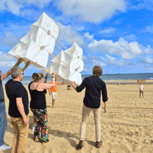 Constructie, samenwerking en plezier staan centraal in de Mega Vlieger Bouwen workshop tijdens een bedrijfsuitje aan zee.
