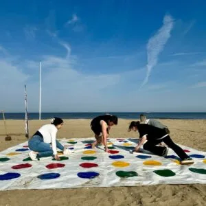 Groep collega’s speelt twister op het strand van Scheveningen tijdens een vrolijk bedrijfsuitje met de Zeskamp activiteit