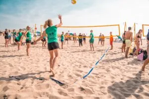Grote groep collega’s speelt beachvolleybal op het zonnige strand van Scheveningen tijdens een sportief en gezellig teamuitje